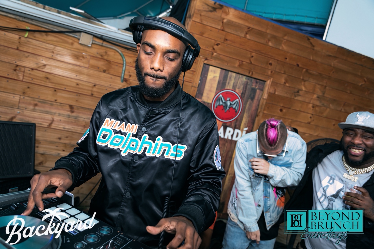 Radio Jamez performing behind the decks wearing a Miami Dolphins jacket
